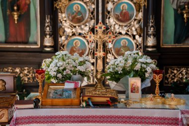Altın haç, beyaz çiçek aranjmanları ve dini simgelerle süslenmiş kutsal bir Ortodoks Hıristiyan sunağı, altın detaylar ve ruhani betimlemelerle süslenmiş bir ikonostaz.