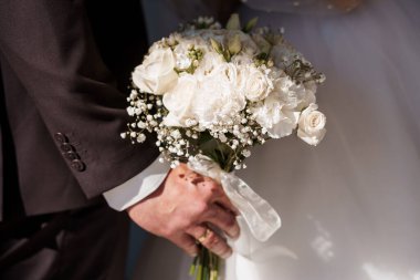 Bir damat, gül ve bebek nefesi ile bembeyaz bir düğün buketi tutuyor. Düğün töreninde romantik bir an sergiliyor. Yumuşak doğal ışık ve rafine edilmiş klasik estetik.