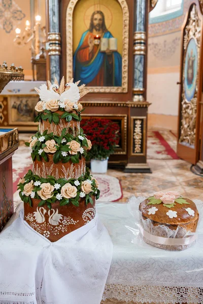 Kuğular, güller ve yeşilliklerle süslenmiş çok katmanlı çok katmanlı güzel bir düğün pastası İsa 'nın süslü bir ikonunun önünde, zengin detaylı bir Ortodoks kilisesinde duruyor.