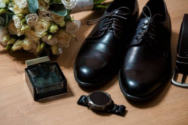 Siyah ayakkabı, beyaz gül buketi, saat, parfüm ve ahşap kemer, düğün için ideal, resmi giysi veya damat hazırlık sahneleri.