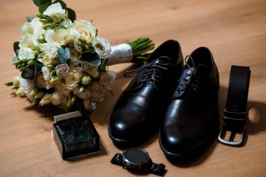 Beyaz bir gül buketi, siyah deri ayakkabı, kemer, saat ve parfüm içeren şık bir damat hazırlığı büyük gün için sofistike ve hazır olmayı iletiyor.