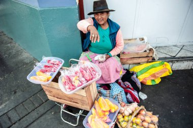 Şehir caddesinde oturan ve meyve satan şapkalı yaşlı etnik kadın, Lima, Peru
