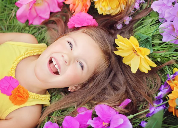 Menina feliz coroa que coloca na grama com flores — Fotografia de Stock