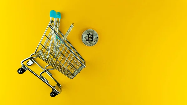 Sarı arka planda bitcoin ve minyatür alışveriş arabasının yukarıdan çekimi. E-ticaret kavramı. 