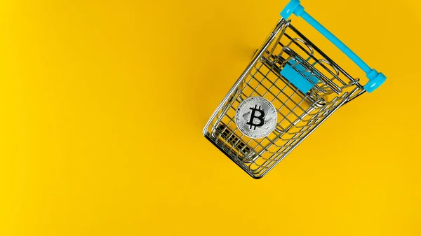 Sarı arka planda minyatür alışveriş arabasının içindeki bitcoin 'in yukarıdan çekimi. E-ticaret kavramı. 