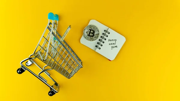Küçük bir alışveriş arabası, bitcoin ve mutlu yıllar içeren küçük bir defter.