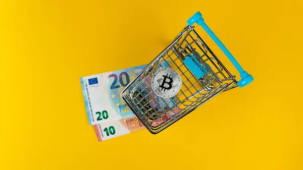 Küçük alışveriş arabasında Bitcoin ve sarı arka planda euro banknotları, genel çekim