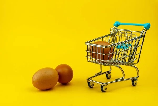 İçinde bir yumurta ve sarı arka planda iki yumurta olan alışveriş arabası.. 