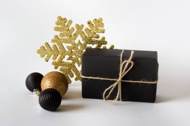 Siyah kağıda sarılı basit bir Noel kompozisyonu. Süslü mücevherler ve beyaz arka planda altın kar tanesi..