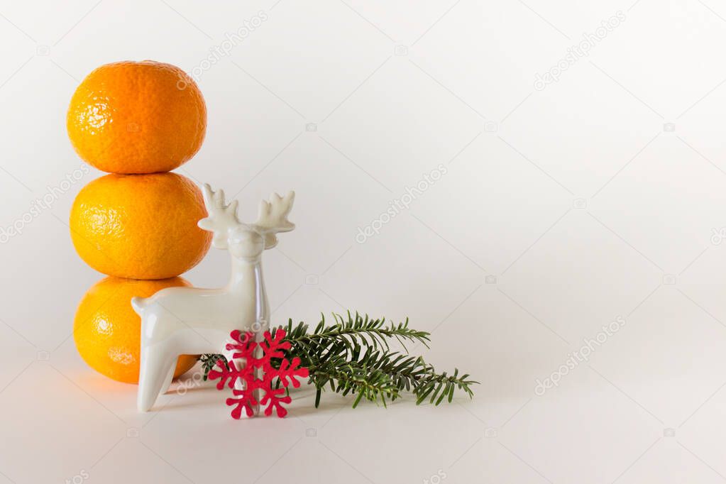 Christmas decor tangerines, evergreen branch and white porcelain reindeer on white background with copy blank space.