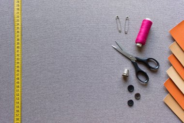 Yapay deri kareler, makas, iğneler, iplikler ve bej kahverengi arkaplan kumaşındaki düğmeler ile model şablonu dikiyorum. Boş alanı kopyalayan fotoğraf.