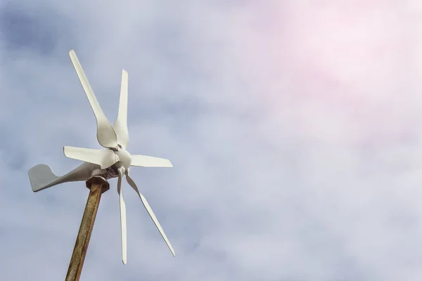 Small windmill wind turbine with blades on the background of sky.
