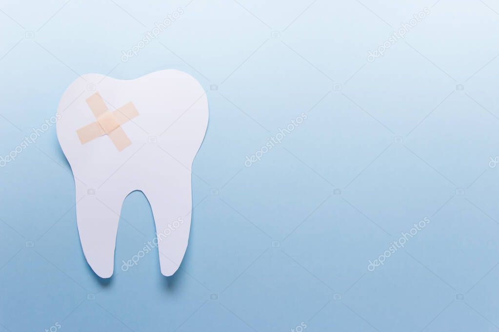 One large paper tooth with patch on blue background. Photo with copy blank space.