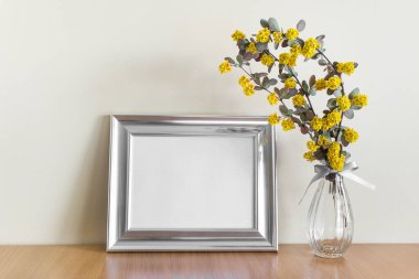 Sanat tasarımı için metalik yatay çerçeve bezi fotoğraf sunumu ve ahşap yüzeyde cam vazoda sarı çiçekler..