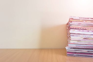 Ahşap yüzeyinde kocaman bir dergi yığını olan basit ofis tarzı kompozisyon. Boş duvarlı resim.