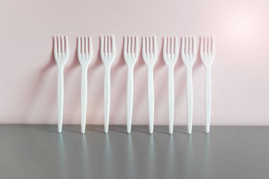 Sarı duvarın yanındaki gri yansıtıcı yüzeyde bir sürü beyaz plastik çatal duruyor..