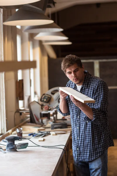 Male carpenter in carpentry workshop blows chips with wooden boa — Stock Image Male carpenter in carpentry workshop blows chips with wooden boa Stock Photo