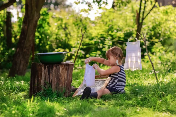 little helper girl washes clothes using the washboard outdoors