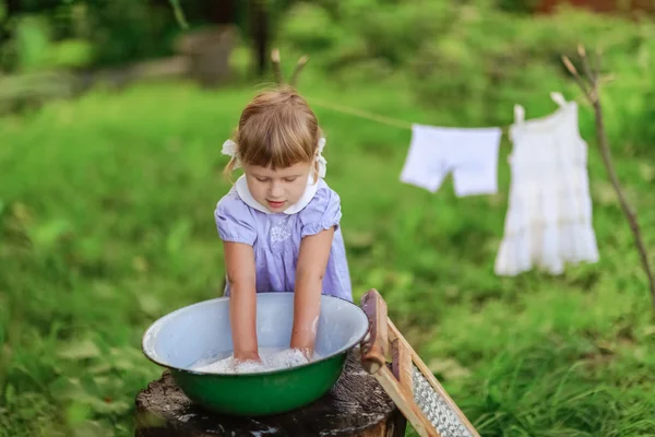 little helper girl washes clothes   in a basin outside