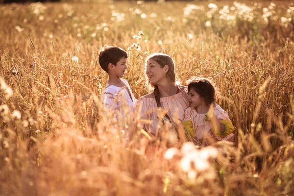 mother hugging her son and daughter in a wheat field