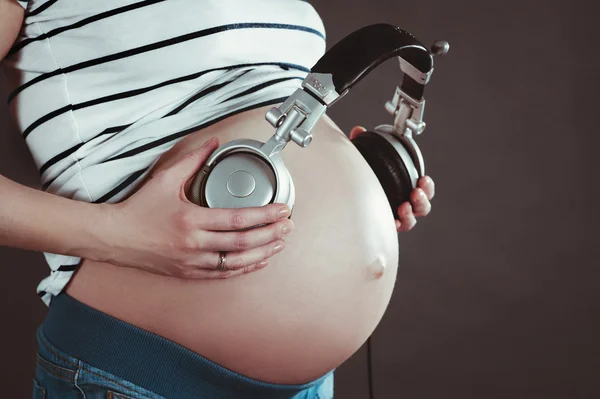 Bauch einer schwangeren Frau. Musik mit Kopfhörern hören. — Stockfoto