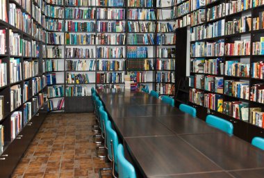 Kütüphanedeki okuma odasında raflarda bir sürü renkli kitap var.