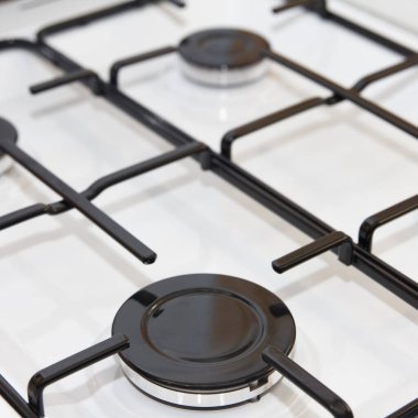 Close-up of a modern gas stove burner with metal grates and control knobs on a white surface