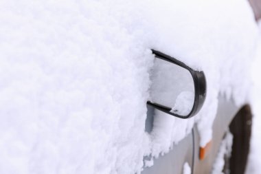 Araba yoğun karla kaplı, yan tarafı görünür ve ayna görünür durumda. Manzara, soğuk hava koşullarını vurgulayarak şiddetli kar yağışı olan bir kış ortamı yakalıyor.