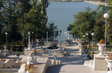 Büyük klasik taş merdiven yeşil bir parktan göle iniyor. Süslü balyalar, çeşmeler ve sokak lambaları yol boyunca dizili. Güçlü gölgelerle güneşli bir gün. Huzurlu, zarif bir ruh hali..