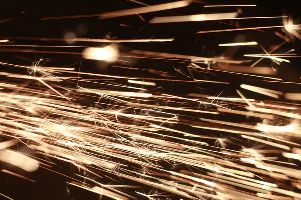 Brillante flujo de chispas en la oscuridad. Fuego chispas sobre un fondo oscuro —  Fotos de Stock