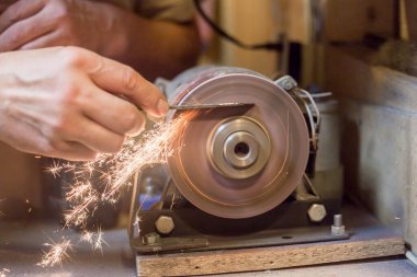 İnsan bir makinede metal bir bıçağı bileyebilir. Adam atölyesinde üretim yapıyor..