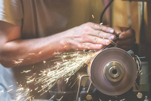 İnsan bir makinede metal bir bıçağı bileyebilir. Adam atölyesinde üretim yapıyor..