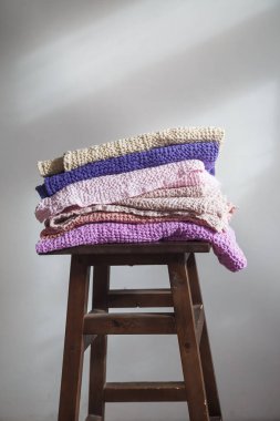 Doğal çarşaf ve pamuktan farklı renkte havlular bir sandalyenin üzerinde.