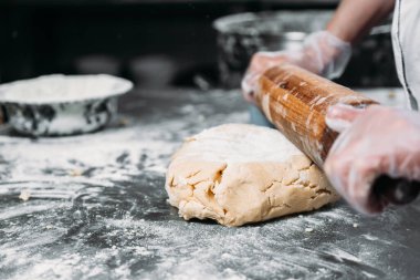 Kadın eli bir hamur yaprağını yuvarlar masanın üzerinde bir mangır ve bir fırın tabağının yanında merdane ile. 