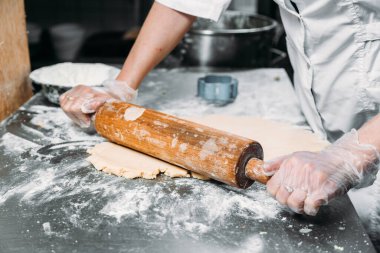 Kadın eli bir hamur yaprağını yuvarlar masanın üzerinde bir mangır ve bir fırın tabağının yanında merdane ile. 