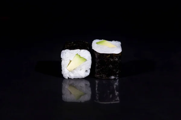 Detailní záběr lahodných sushi rohlíků na černé lesklé desce. Horizontální fotografie potravin na černém pozadí. — Stock fotografie