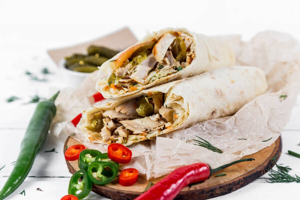 Shawarma with chicken, with sauce, onions, pickles, herbs and hot red pepper on a light background