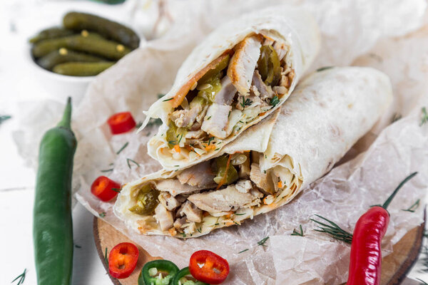 Shawarma with chicken, with sauce, onions, pickles, herbs and hot red pepper on a light background