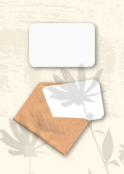 Sebuah amplop dengan dua lembar kertas putih bertekstur pada latar belakang kuning meja. Mockup overlay dengan bayangan tanaman. Cahaya alami melemparkan bayangan dari bunga artichoke Yerusalem — Stok Foto