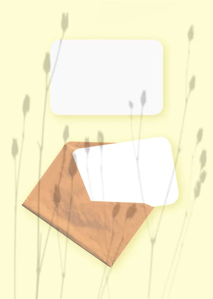 Mockup mit einer Überlagerung von Pflanzenschatten auf einem Umschlag mit zwei Blättern strukturiertem weißem Papier auf gelbem Tischhintergrund. Vertikale Orientierung — Stockfoto