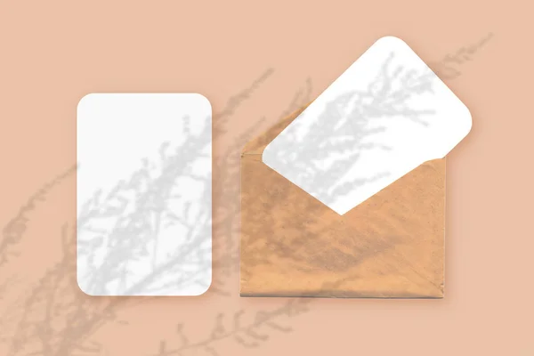 Mockup dengan lapisan bayangan tanaman pada amplop dengan dua lembar kertas putih bertekstur pada latar belakang meja oranye. Orientasi horisontal — Stok Foto
