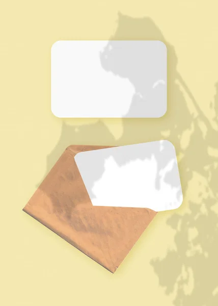 Mockup növényi árnyalatokkal a borítékon, két lap texturált fehér papírral, sárga asztali háttérrel. Függőleges irány — Stock Fotó