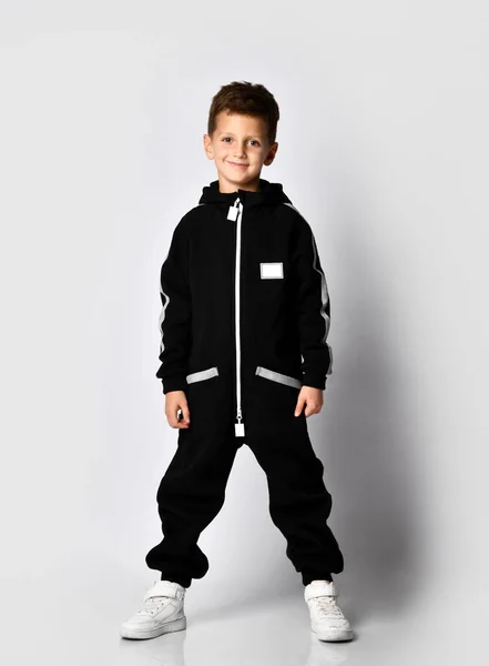 Little brunette kid in colorful tracksuit and sneakers on a gray background. — Stock Photo, Image