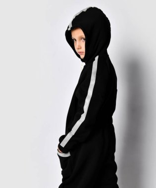 Şık bir çocuk, kamuflajlı, kalın bir sonbahar elbisesi giymiş, tulumlu, yarım bir dönüş yapıyor, omzunun üstünden bakıyor.