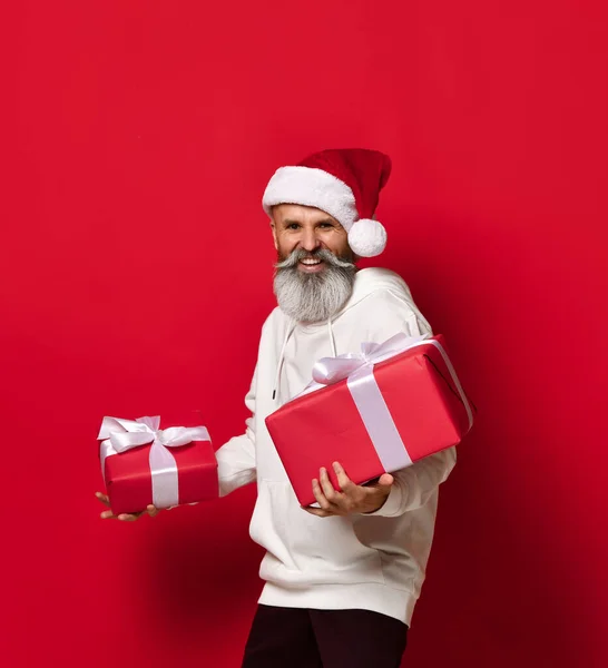 Homme dans un chapeau de Père Noël avec une expression surprise et embarrassée regarde les cadeaux. — Photo
