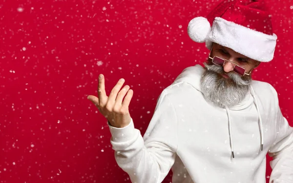 Hipster senior dans un chapeau Santa clins d'oeil et les appels avec son doigt appelant à des réductions de Nouvel An. — Photo