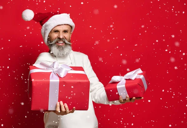 Homme dans un chapeau de Père Noël avec une expression surprise et embarrassée regarde les cadeaux. — Photo