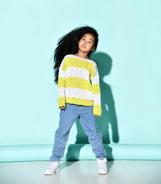 小さなブルネット女の子でA明るいセーターとジーンズshakes彼女の頭と髪. — ストック写真