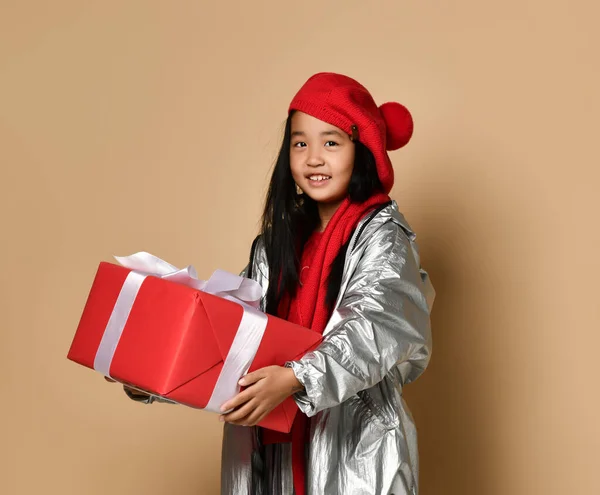 Koreaans meisje houdt een groot rood cadeau met een witte strik en kijkt naar de vrije ruimte voor tekst. — Stockfoto