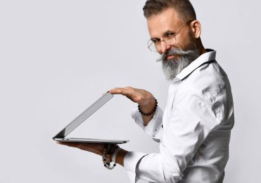 Beyaz tişörtlü, sakallı, olgun bir adam sinsi bir gülümsemeyle bilgisayarı gri arka planda kapatıyor..